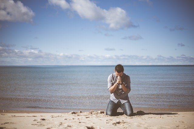 Muž sa modlí na pláži pri mori 